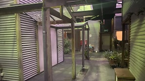 An indoor corridor with closed shuttered storefronts, a metal structure, and potted plants.