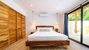 Ein Schlafzimmer mit einem hölzernen Bettgestell, einem großen Fenster mit Blick ins Grüne und einem Holzschrank.