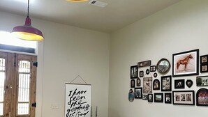 A cozy living room with a white sofa, a wooden coffee table with books, a wooden door, and a wall decorated with framed pictures.
