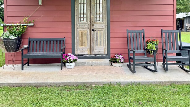 A red building with a wooden porch, two benches, and potted plants.