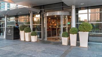 Entrada moderna de hotel com porta giratória, portas de vidro e plantas em vasos.