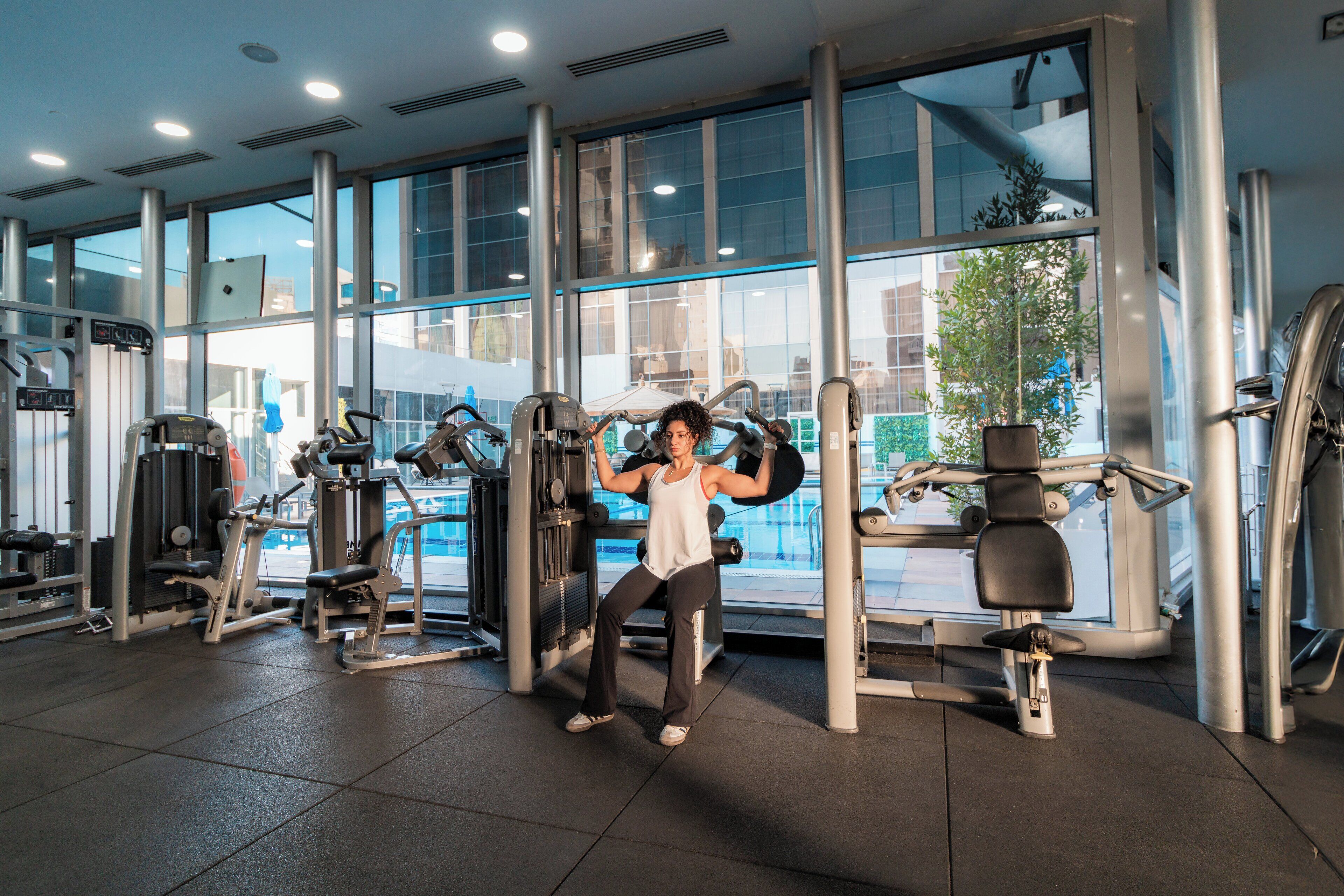 Un gimnasio con diversas máquinas de ejercicio, amplias ventanas y vistas al exterior.