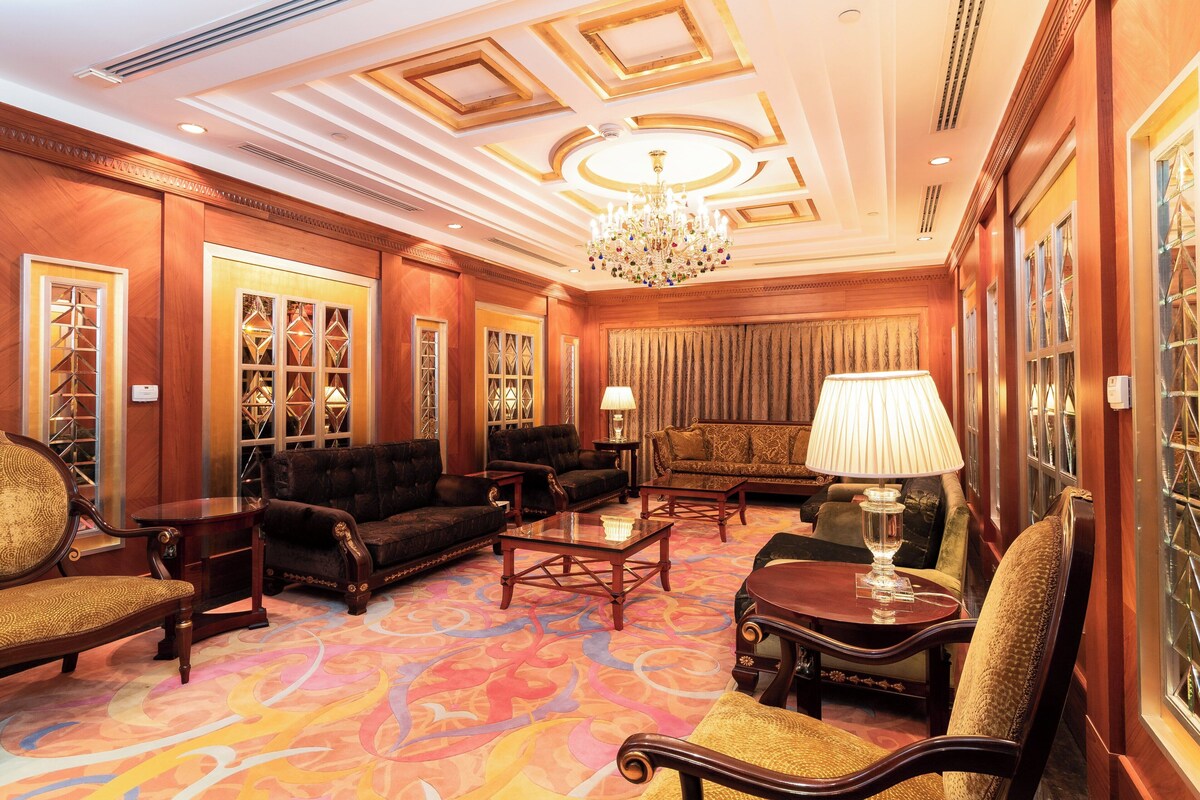 A luxurious room with a large chandelier, plush seating, and a patterned carpet.