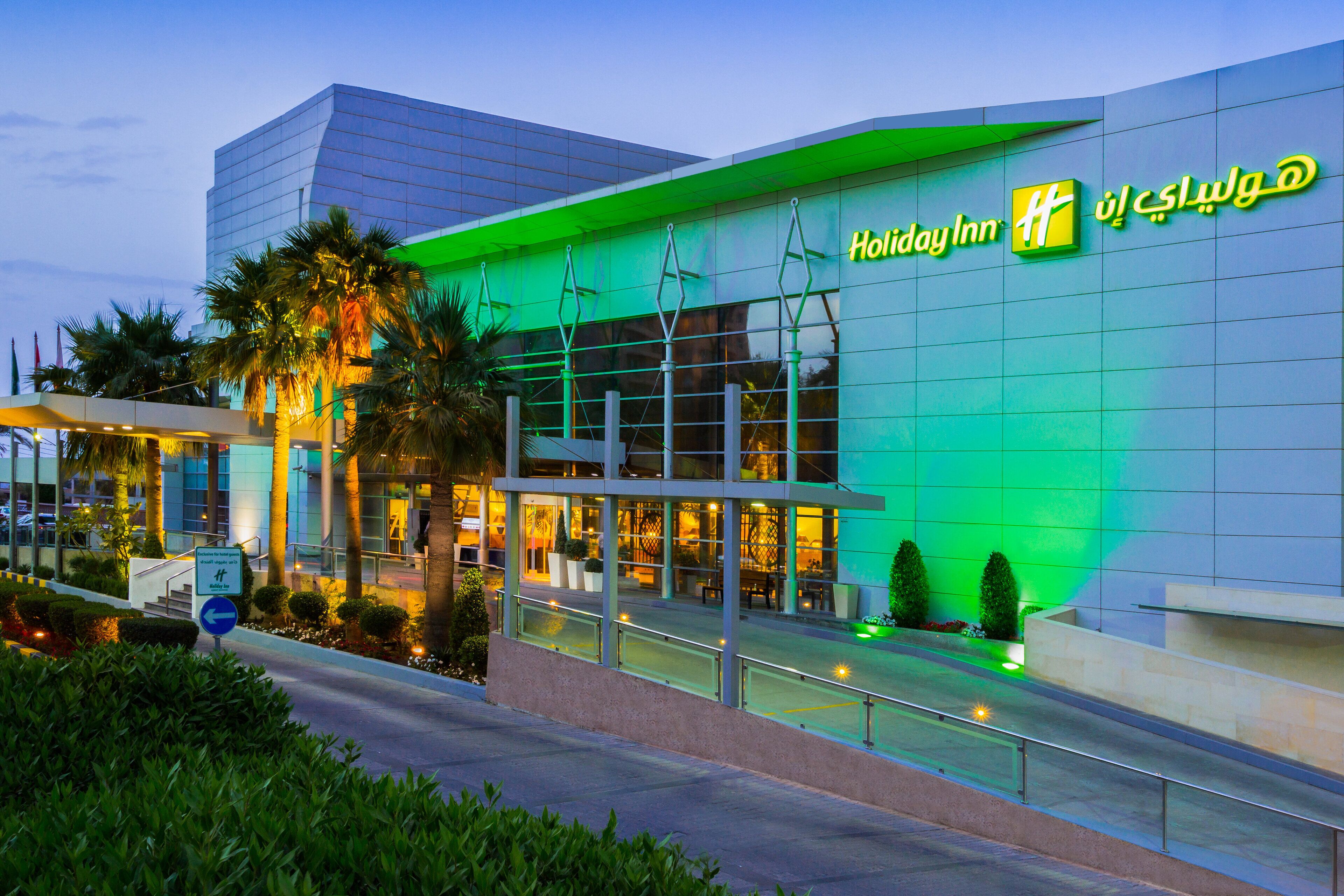 Un hotel Holiday Inn con fachada de vidrio moderna y detalles de iluminación verde.