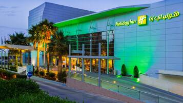 Un hotel Holiday Inn con fachada de vidrio moderna y detalles de iluminación verde.