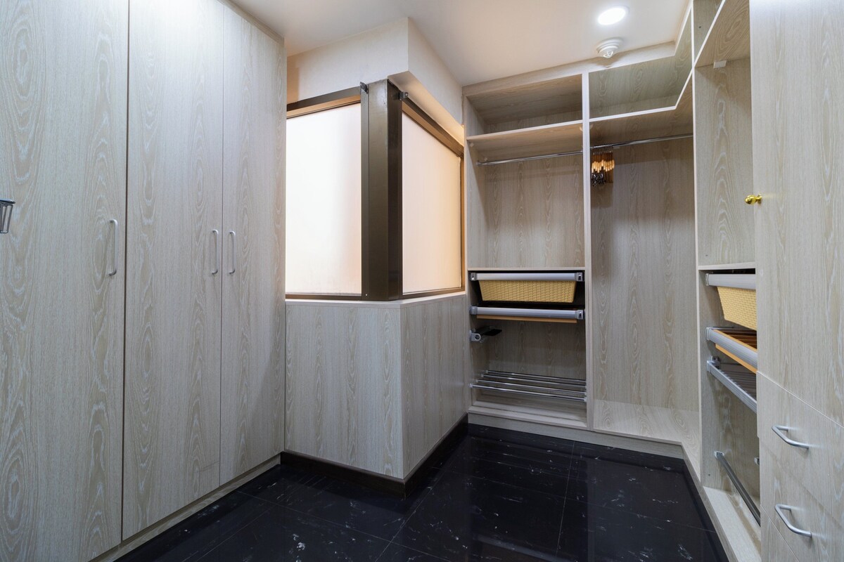 A modern closet with wooden doors, a metal shelf, and a black tiled floor.