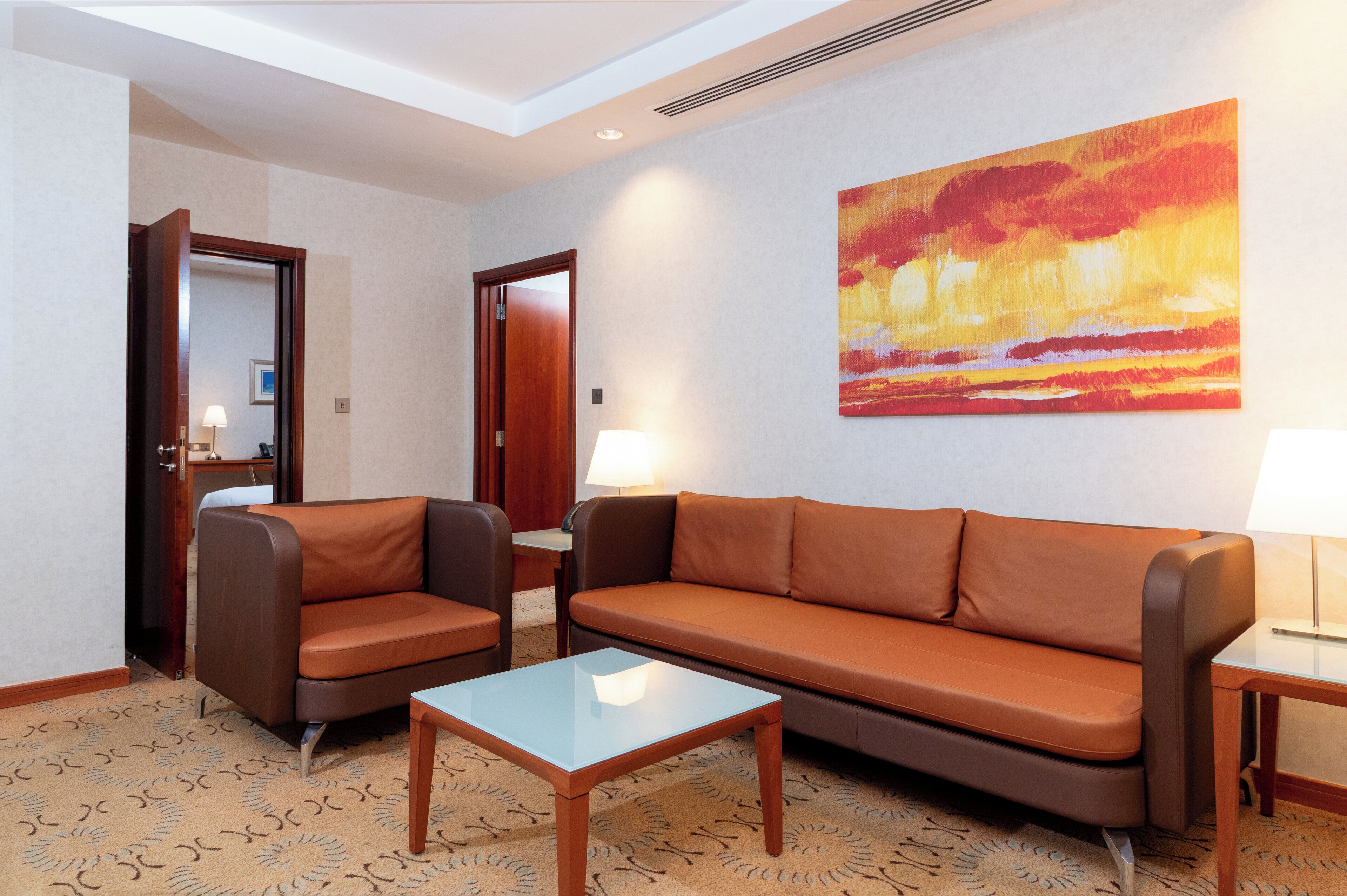 Una sala de estar moderna con un sofá, dos sillones, una mesa de centro de vidrio y un cuadro en la pared.