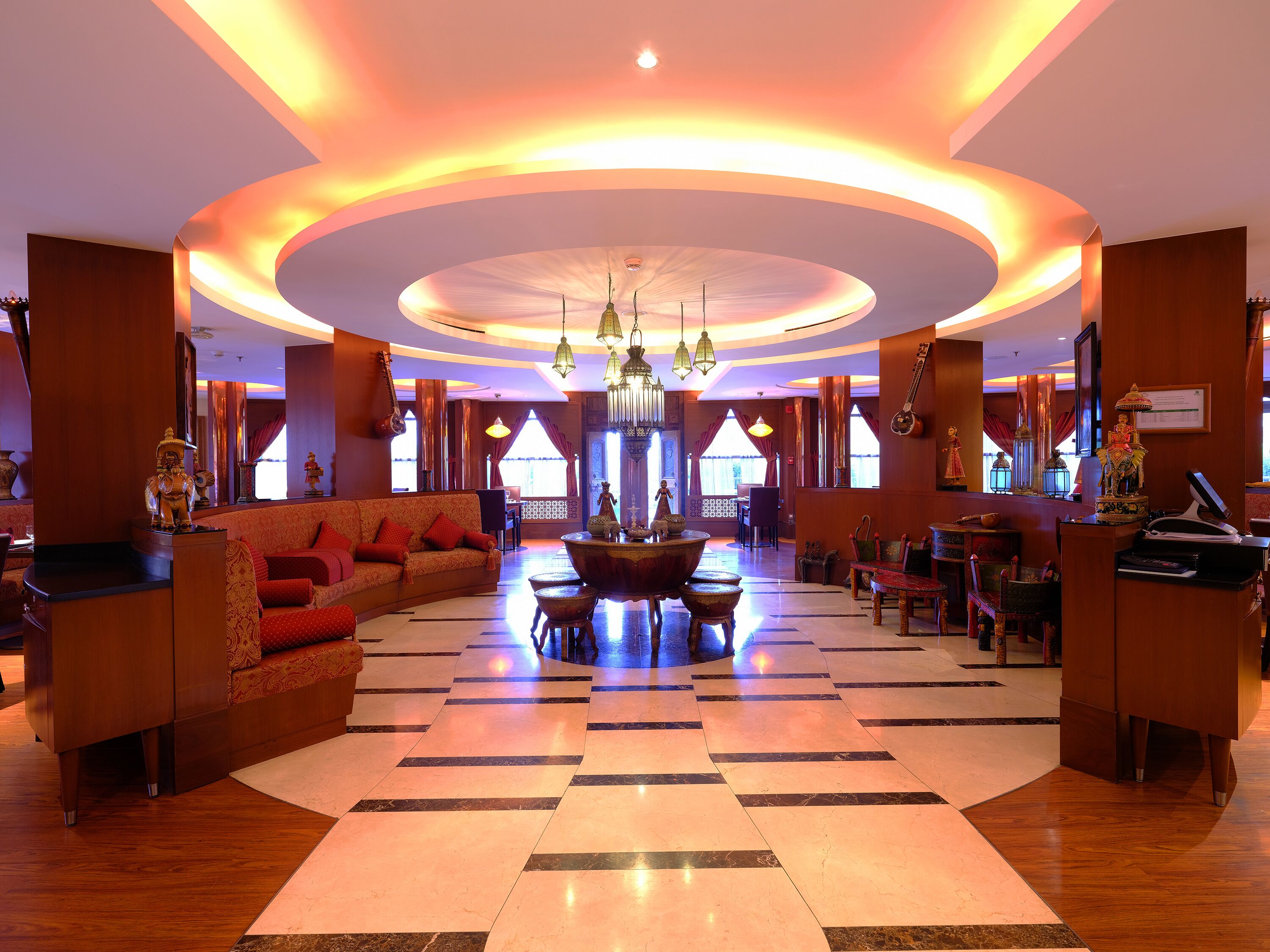 A spacious lobby with a checkered floor, a central seating area, and a ceiling with circular lighting.