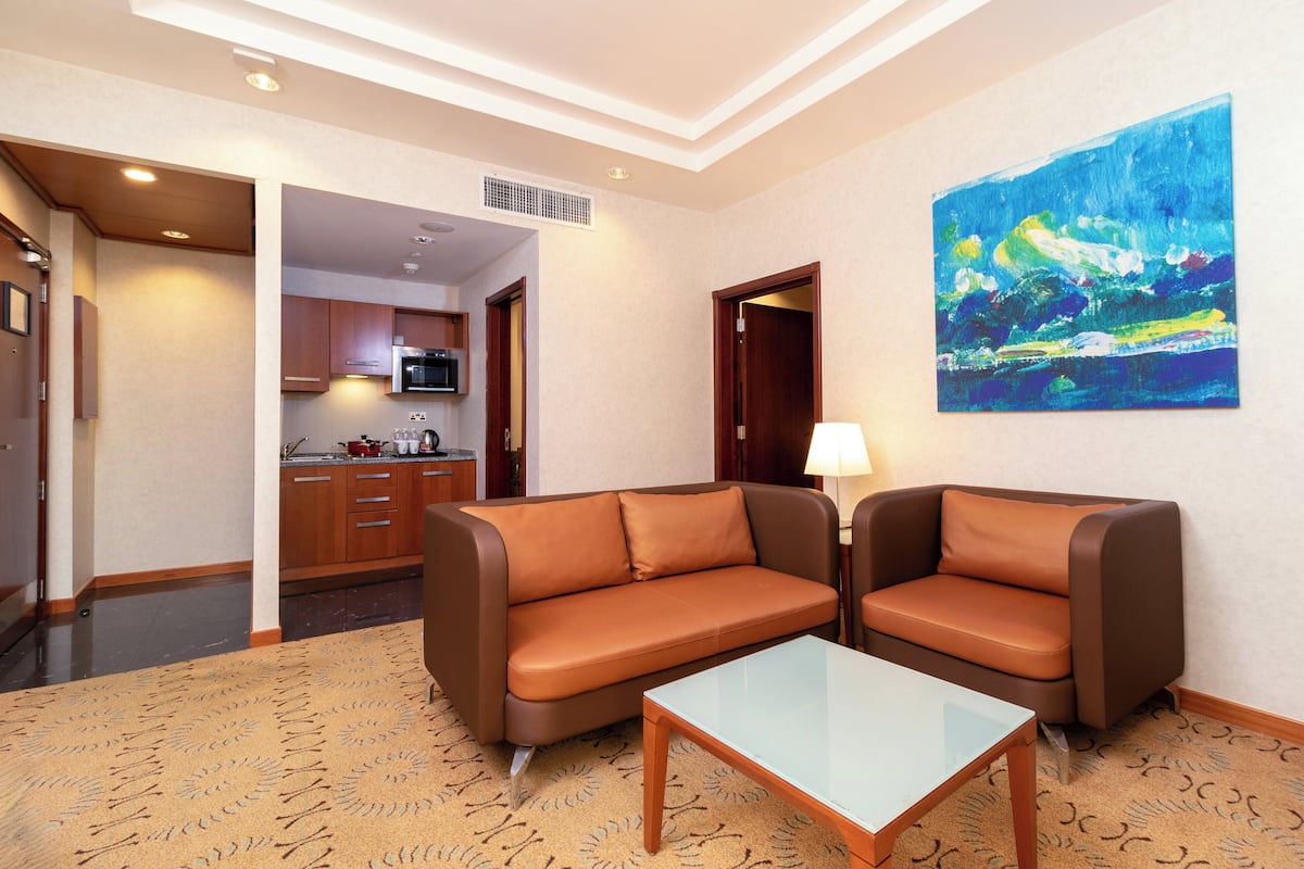A hotel room with a brown leather sofa, a glass coffee table, and a painting on the wall.