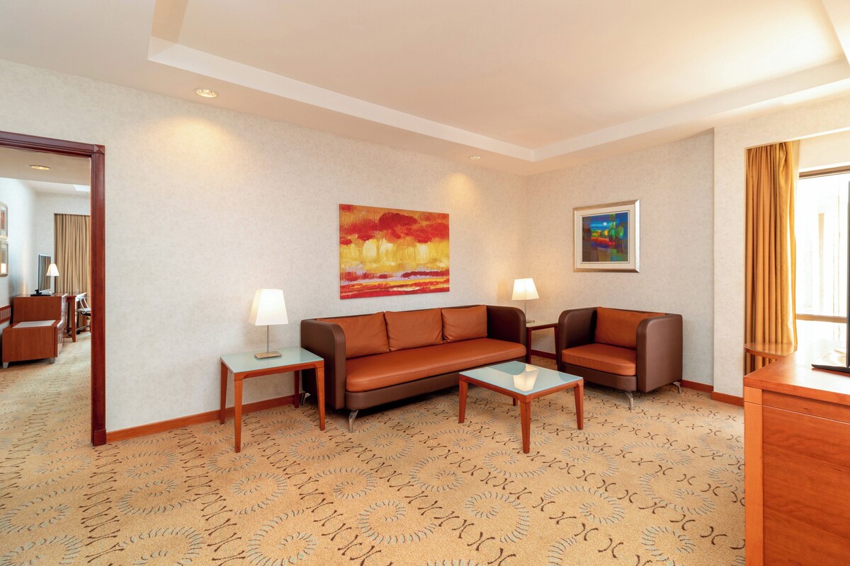 A hotel room with a sofa, two side tables, a coffee table, and a painting on the wall.