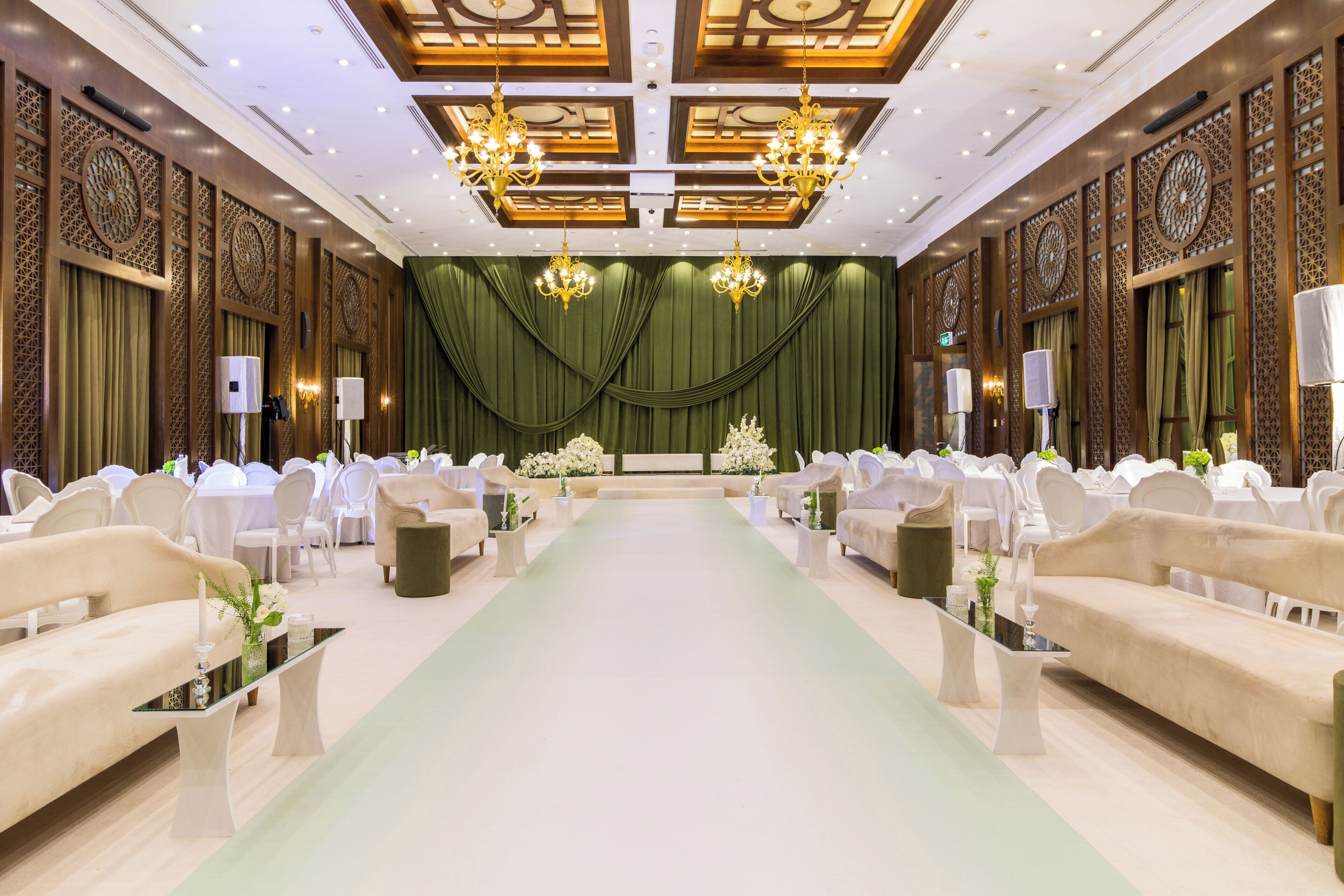 A formal event space with a green carpet, white chairs, and chandeliers.
