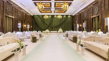 A formal event space with a green carpet, white chairs, and chandeliers.