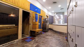 A sauna area with wooden benches, a bench, a refrigerator, and lockers.