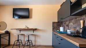 A compact kitchen with a flat-screen TV, two stools, and a wooden countertop. - Savčić Apartmani (Petrovac)