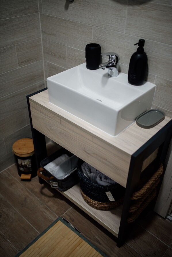 A bathroom with a white sink, black soap dispenser, and a small trash bin. - Savčić Apartmani (Petrovac)