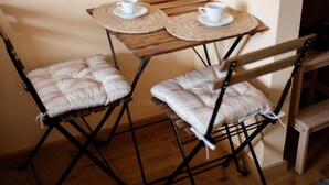 A small wooden table with two white cups and a placemat, flanked by two cushioned chairs with metal frames. - Savčić Apartmani (Petrovac)