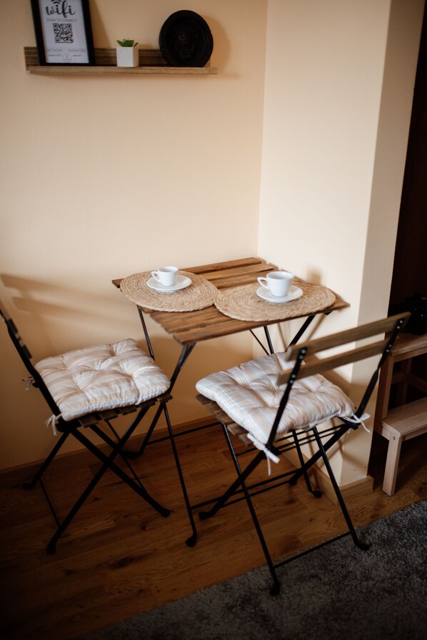 Una pequeña mesa de madera con dos tazas blancas y un mantel individual, flanqueada por dos sillas con cojines y estructura de metal.
