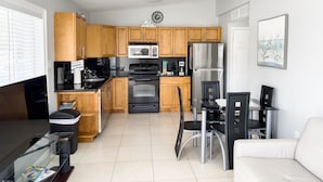 A modern kitchen with wooden cabinets, a black countertop, stainless steel appliances, and a dining area with a white sofa and chairs. - Beautiful Condo Two Blocks to The Beach ! (Cape Canaveral)