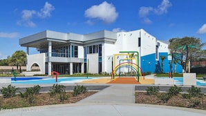A modern building with a large glass facade, a covered entrance, and a colorful playground area. - Beautiful Condo Two Blocks to The Beach ! (Cape Canaveral)