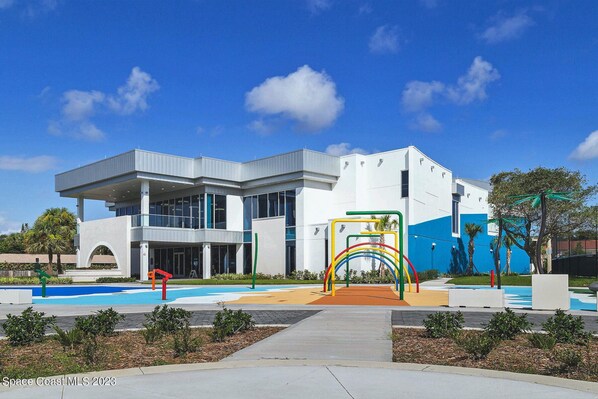 A modern building with a large glass facade, a covered entrance, and a colorful playground area.