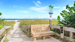 A wooden bench on a boardwalk leading to a beach, with a sign about sea turtle nesting season. - Beautiful Condo Two Blocks to The Beach ! (Cape Canaveral)