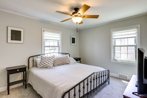 A bedroom with a bed, a ceiling fan, two bedside tables, and a TV.