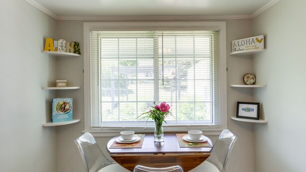 Un comedor con una mesa de madera, dos sillas, un jarrón con flores y estanterías con libros y objetos decorativos.