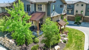 A multi-story residential building with a covered porch, stone retaining wall, and landscaped garden. - Experience mountain views at Blackstone Escape, a spacious 3BR townhouse in Park City. (Park City)