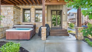 A modern outdoor patio with a hot tub, a covered grill, and a stone pillar. - Experience mountain views at Blackstone Escape, a spacious 3BR townhouse in Park City. (Park City)