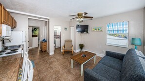 A compact living space with a kitchenette, a dining area, a TV mounted on the wall, and a ceiling fan. - Blue Water Beach Rental #6   A little slice of beach paradise (Indian Rocks Beach)