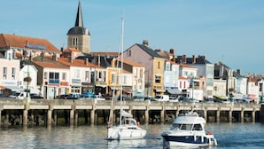 Un pueblo costero con edificios coloridos, una aguja de iglesia y barcos amarrados en el muelle.