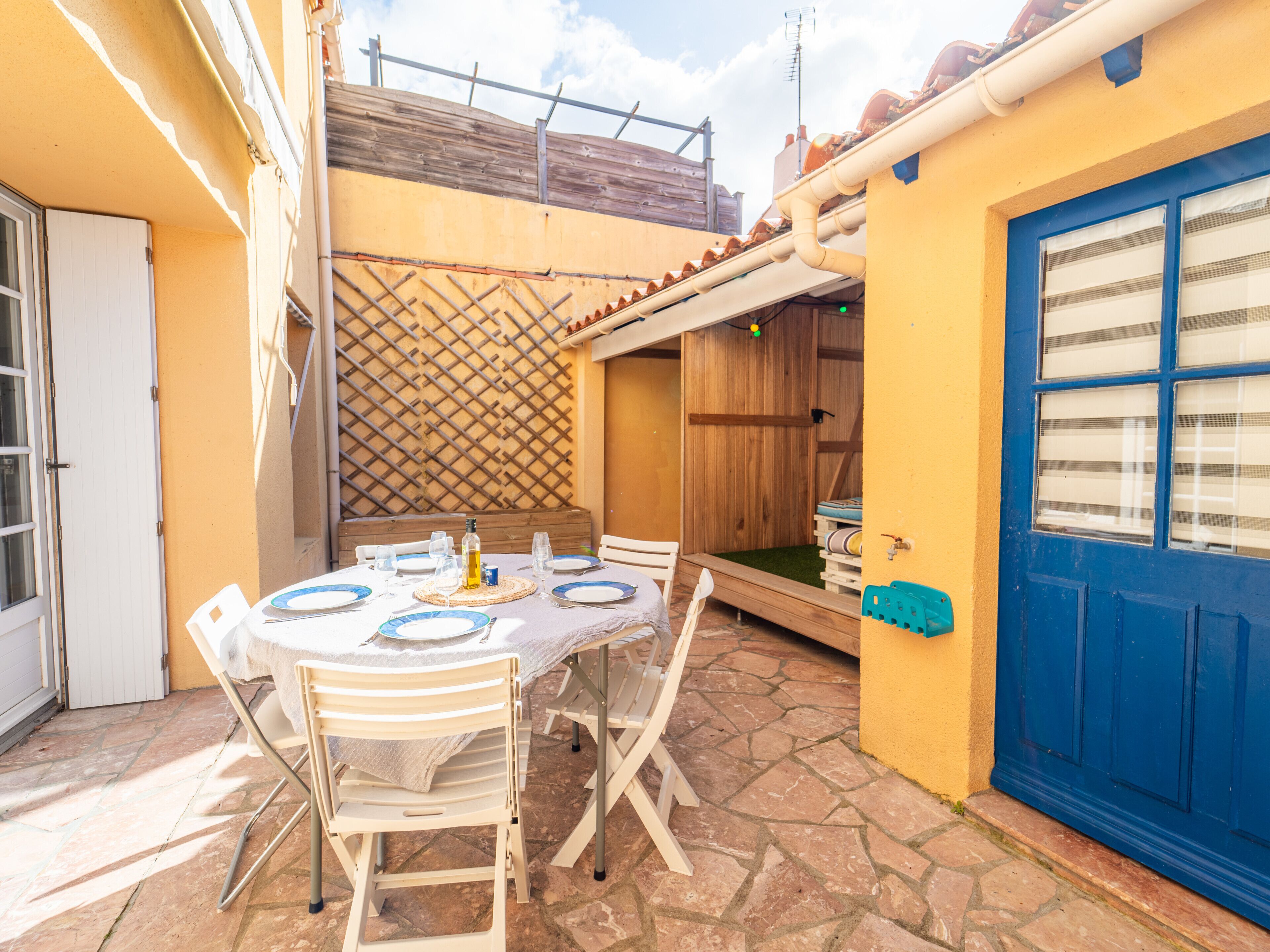 An outdoor patio with a table set for dining, surrounded by chairs, and a blue door with windows.