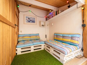Una habitación acogedora con dos camas sobre palets de madera, un pequeño estante con libros y un cuadro en la pared.