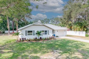 A single-story house with a gabled roof, a front garage, and a well-maintained lawn with various plants. - TOOTSIE’S BEACHSIDE POOL COTTAGE (Seminole)