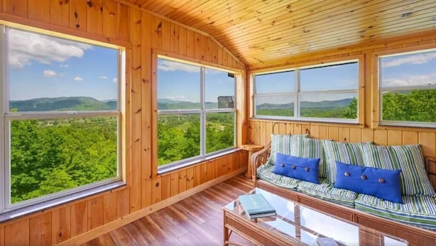 A wooden cabin with large windows offering views of a green landscape. - Little Greenbriar Lodge: Free Attraction Tickets, Hot Tub, Mtn Views & Adjacent National Park (Sevierville)