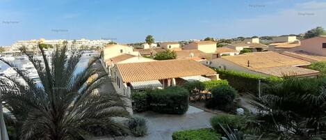 A residential area with terracotta-roofed houses, a marina with boats, and palm trees.