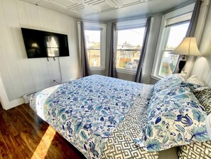 A bedroom with a bed, a TV mounted on the wall, and windows with curtains.