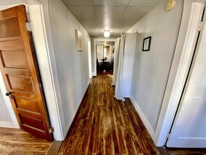 A hallway with wooden flooring, white walls, and a ceiling light.