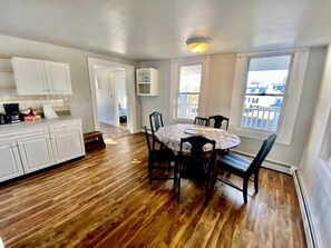 A kitchen with white cabinets, a dining table with chairs, and a view of the outside through windows.