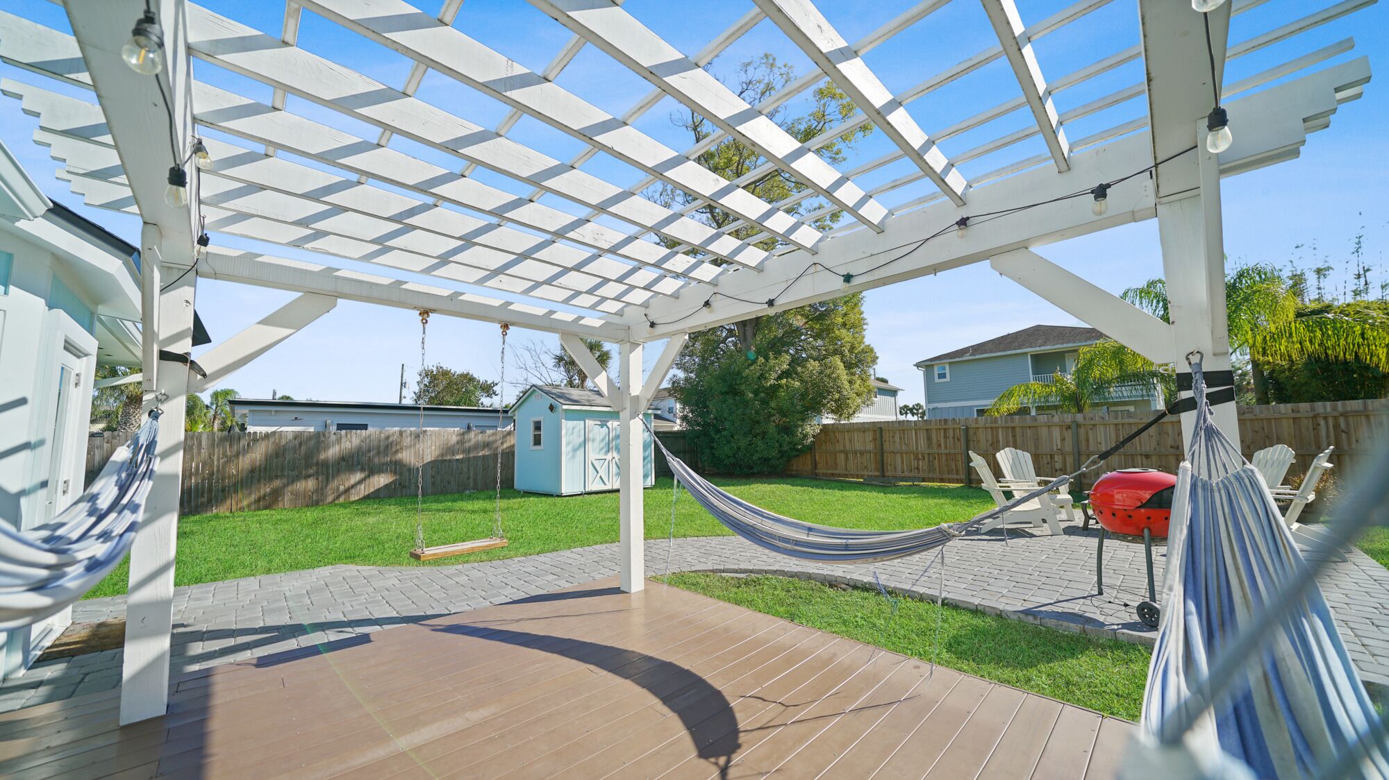 Un patio couvert avec un hamac, une balançoire et une terrasse en bois.