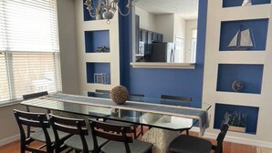 Un'area pranzo con tavolo in vetro e sedie scure, un lampadario e una parete azzurra con mensole.