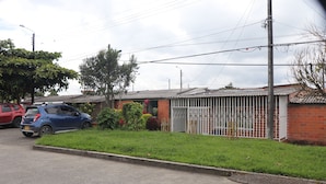 A residential street with a blue car parked on the side, a red car in the background, and a gated house with a metal fence. - Casa Hotel ivanna (Montenegro)