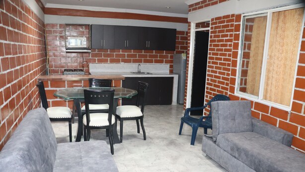 A compact kitchen with dark cabinets and a microwave, a dining table with chairs, and a grey sofa. - Casa Hotel ivanna (Montenegro)