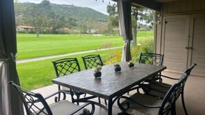 En täckt uteplats med ett bord och stolar, med utsikt över ett grönskande landskap med kullar.