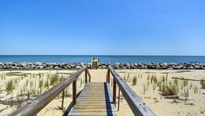 A wooden boardwalk leading to a beach with a rocky shoreline and clear blue sky.