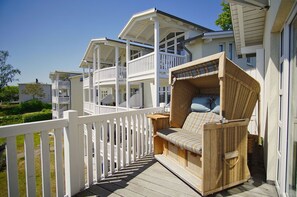 A wooden deck with a wicker sofa and a white picket fence. - Die Ferienwohnung Nr. 51 in den Meeresblick Residenzen - Meeresblick (Göhren)