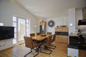 A modern kitchen with a wooden dining table, chairs, and a built-in oven. - Die Ferienwohnung Nr. 51 in den Meeresblick Residenzen - Meeresblick (Göhren)