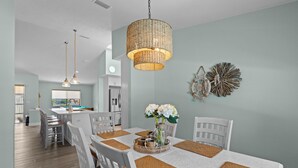 A dining area with a table set for six, surrounded by white chairs, a woven centerpiece, and a large woven pendant light. - Manatees Coming Waterfront Deep canal.Gulf access.Pool home! Pool table.Sleeps8. (Crystal River)