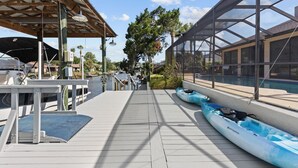 A boat dock with kayaks lined up, a covered seating area, and a view of the water and buildings in the background. - Manatees Coming Waterfront Deep canal.Gulf access.Pool home! Pool table.Sleeps8. (Crystal River)