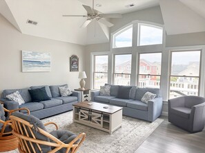A spacious living room with a grey sofa set, a wooden coffee table, and a wicker chair. - Seven Sisters 26: Oceanside, hot tub, community pool, easy beach access. (Nags Head)